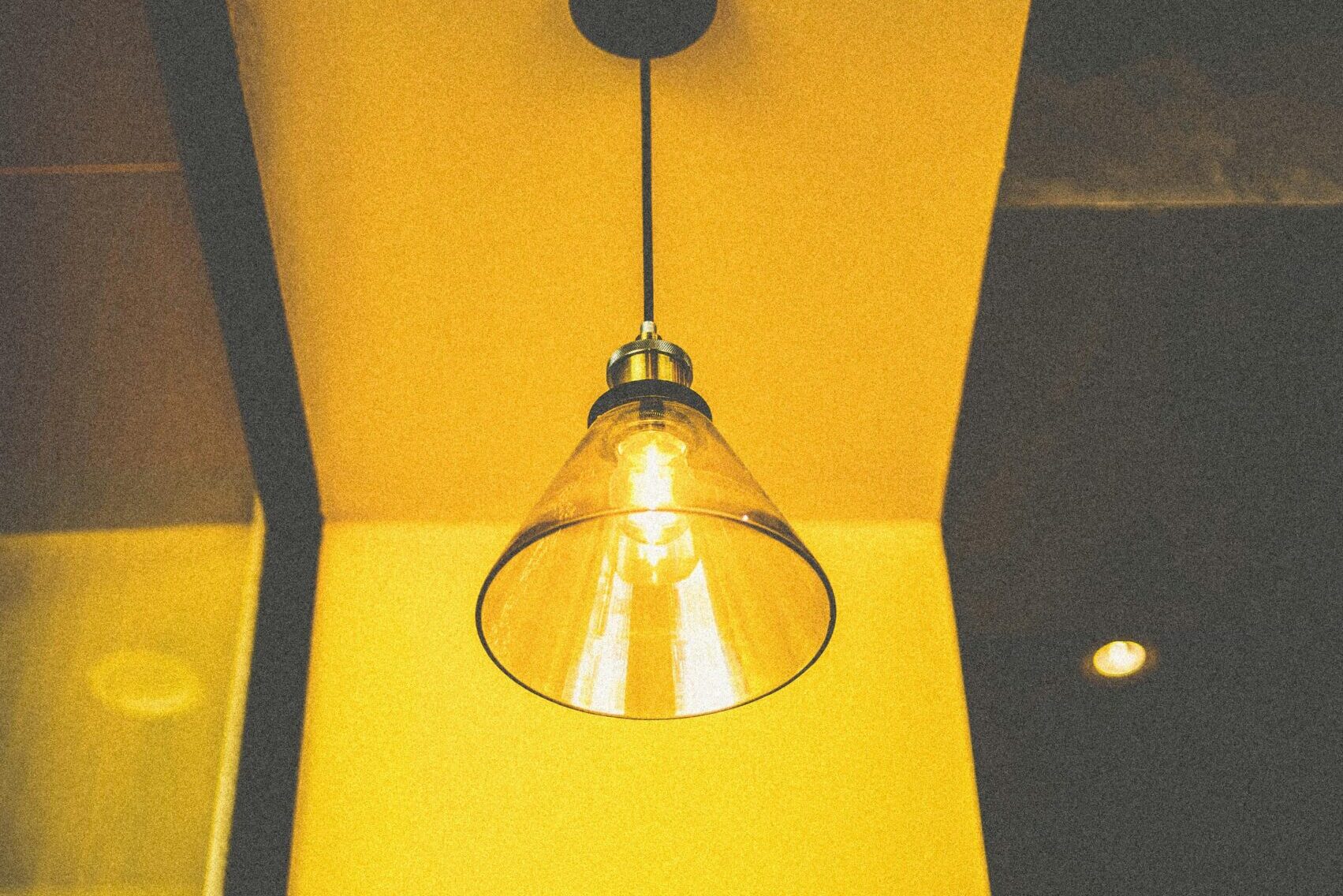 A warm pendant light with a clear glass shade hanging from a yellow ceiling.